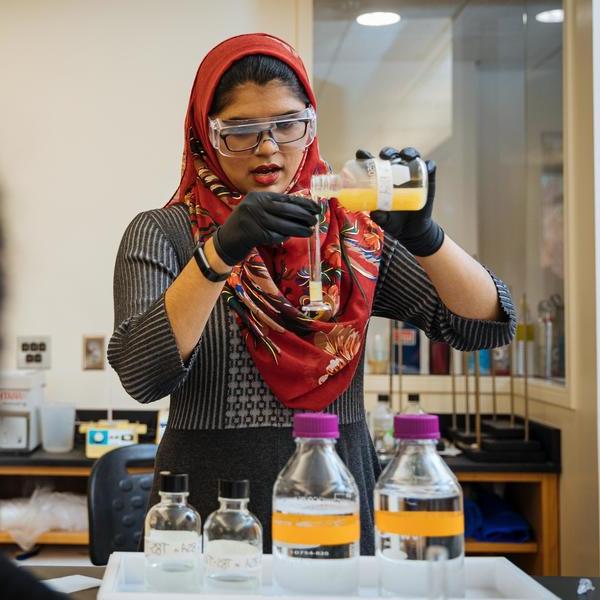 A chemistry major student wearing a colorful hijab pours a solution into a test tube.