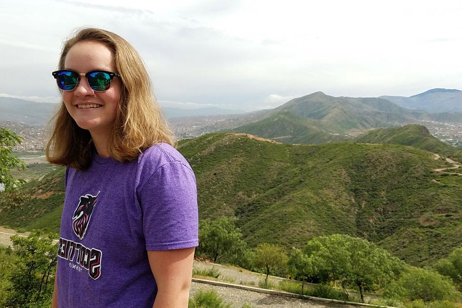 艾格尼丝·斯科特是一名留学生，她戴着墨镜，微笑着站在玻利维亚一座绿色的山顶上.